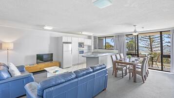 A modern living room with a blue sofa, a TV, and a dining area with a table and chairs.