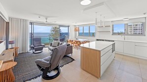 A modern living room with a view of the sea, a dining area, and a kitchen with white cabinetry. - Northwind Holiday Apartments Mooloolaba (Mooloolaba)