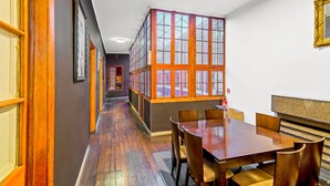 A hallway with wooden flooring, a dining area with a wooden table and chairs, and a large window with multiple panes. - La Chimba Hostel (Santiago)
