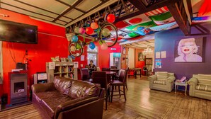 A cozy lounge area with leather sofas, a fireplace, and a ceiling adorned with colorful decorations. - La Chimba Hostel (Santiago)