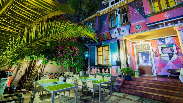 A colorful building with a patio area featuring tables and chairs. - La Chimba Hostel (Santiago)