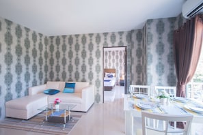Una sala de estar moderna con un sofá, una mesa de centro y un comedor. Se ve una cama al fondo.
