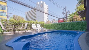 A swimming pool with lounge chairs and a hedge, surrounded by buildings and power lines. - Grande Elegance Serviced Apartment (Patong)