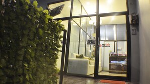 A hotel entrance with a glass door, a sign indicating the hotel is open, and a visible interior with a white sofa and a Christmas tree. - Grande Elegance Serviced Apartment (Patong)