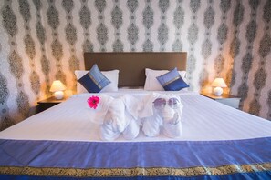 Una cama bien hecha con toallas, una flor, dos almohadas y una mesita de noche con una lámpara.