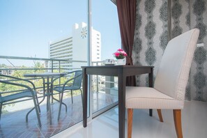 A balcony with a table and chairs, a potted plant, and a view of buildings. - Grande Elegance Serviced Apartment (Patong)