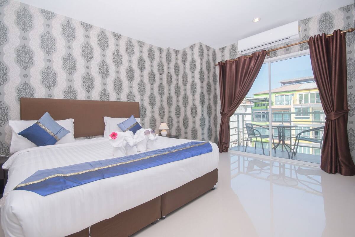 Een hotelkamer met een groot bed, een balkon met uitzicht op gebouwen en behang met een patroon.