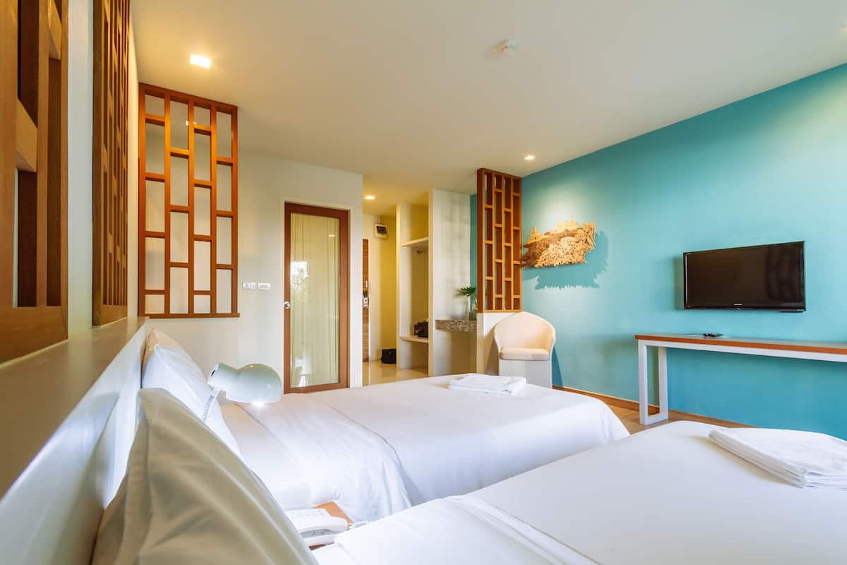 A hotel room with two beds, a TV, a desk, and a bathroom visible through an open door.