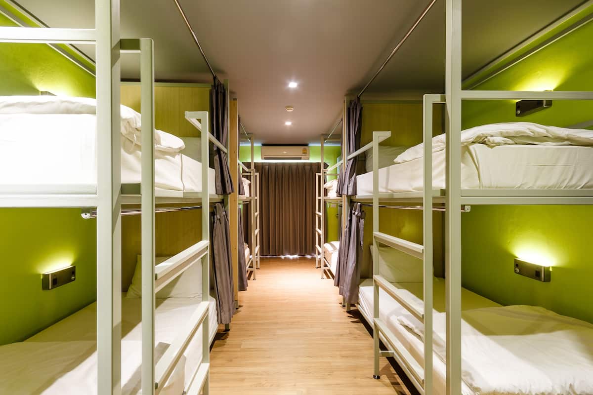 A narrow corridor with bunk beds on either side, a wooden floor, and a curtain at the end.