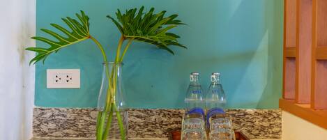 A kitchen counter with a vase containing green plants, a tray with glasses, and a blue wall with a power outlet.