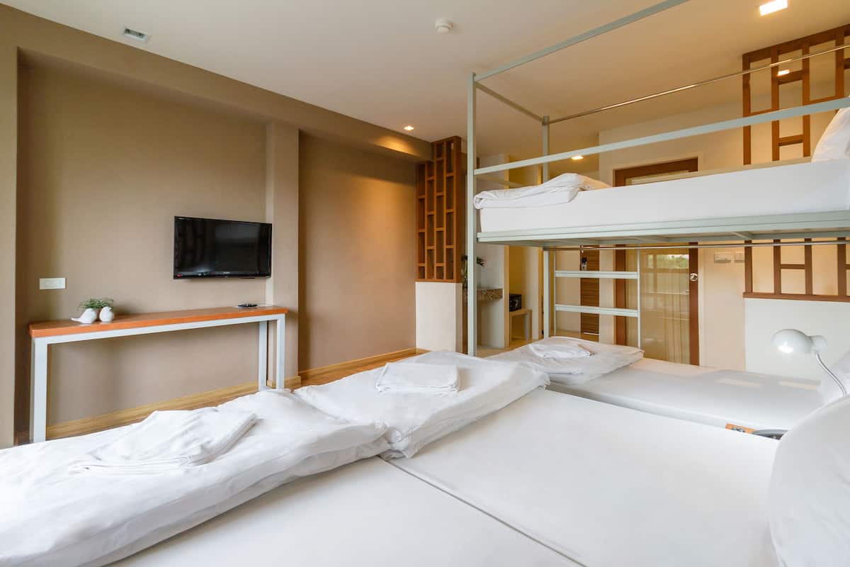 A hotel room with a bunk bed, a flat bed, a TV, a bedside table, and a mirror.