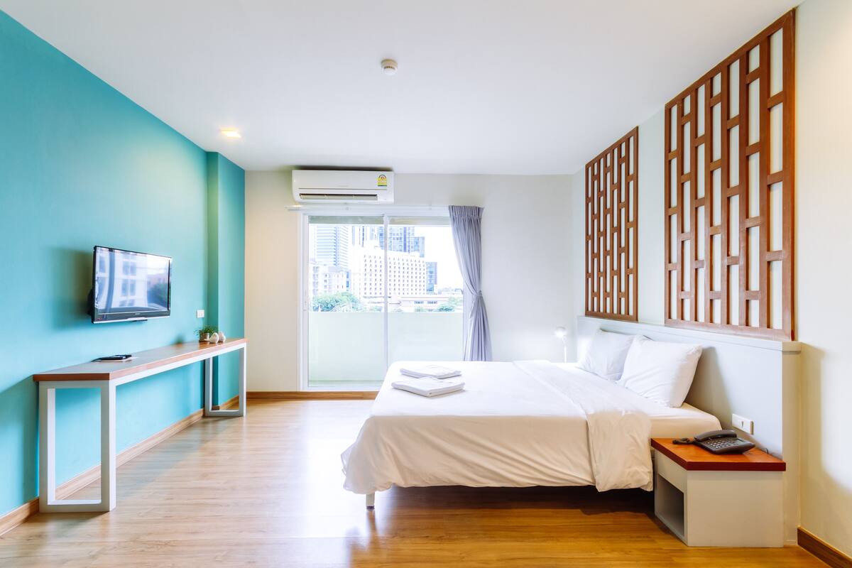 A hotel room with a bed, a desk, a TV, and an air conditioning unit.
