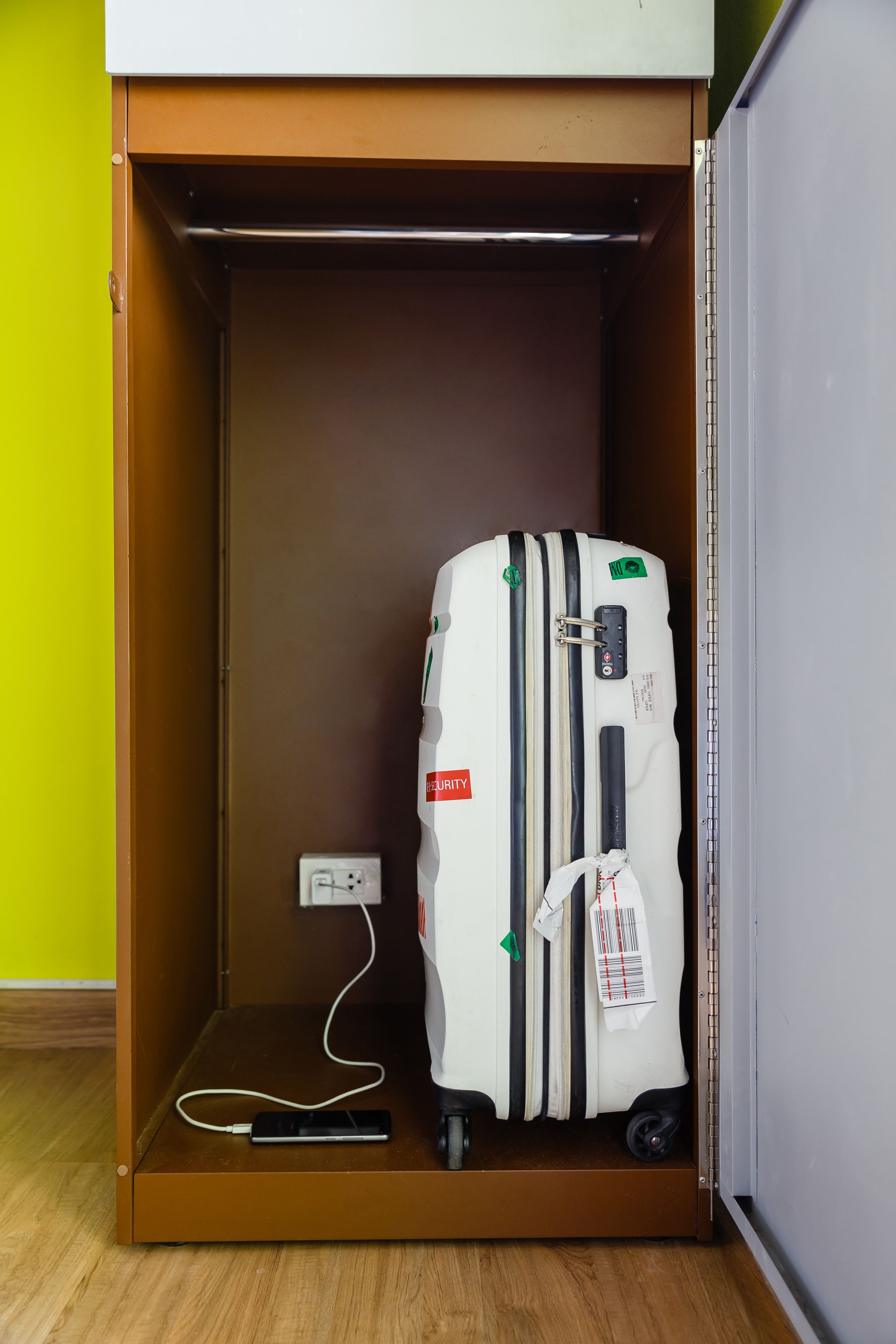A suitcase in a compartment of a cabinet with a power outlet and a cable.