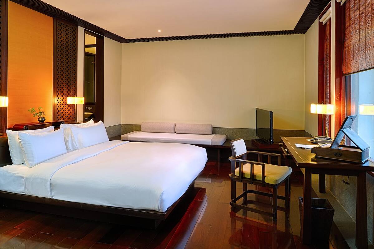 Quarto de hotel com uma cama grande, um sofá, uma escrivaninha com cadeira e uma televisão.