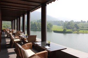 Un espace extérieur aménagé, abrité et doté de mobilier en osier, offrant une vue sur un lac et des montagnes.