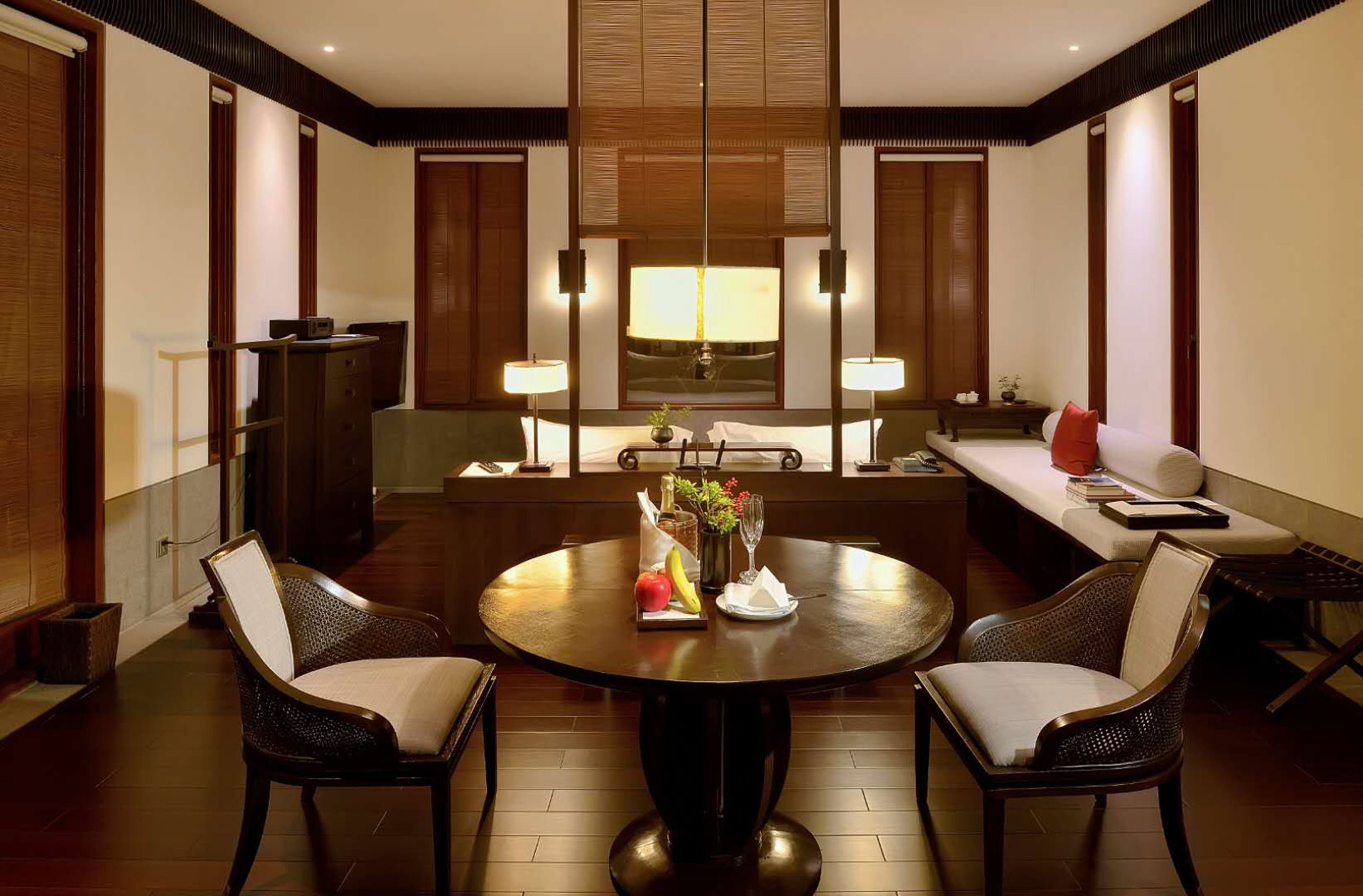 A modern hotel room with a round dining table, two chairs, a sofa, and a small side table.