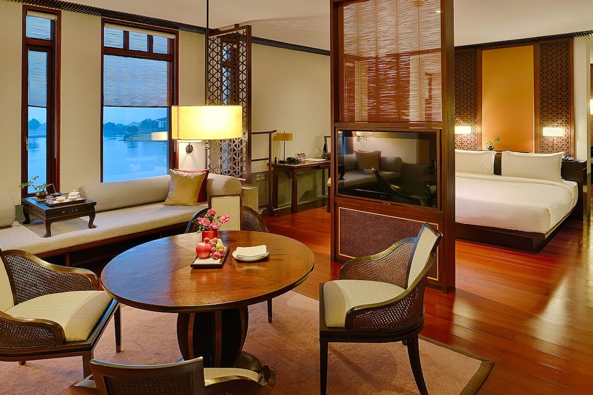 Quarto de hotel com sofá, mesa de jantar redonda, duas cadeiras, televisão, cama e vista para o exterior.