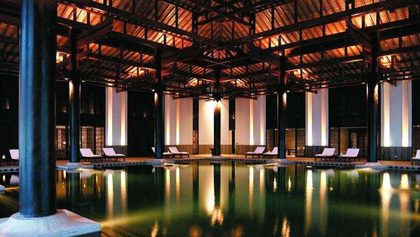 Una amplia piscina cubierta con sillones de descanso y un techo alto con vigas de madera.