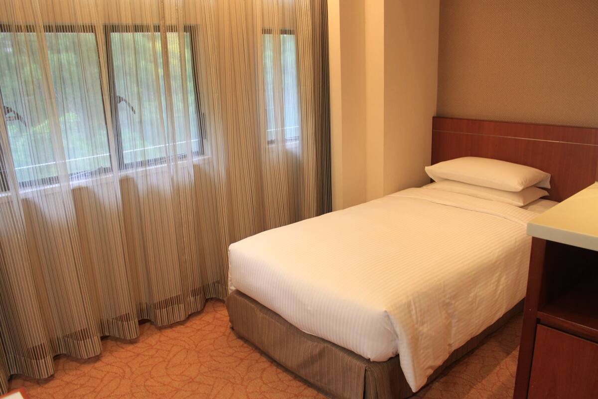 A hotel room with a bed, curtains, and a wooden headboard.