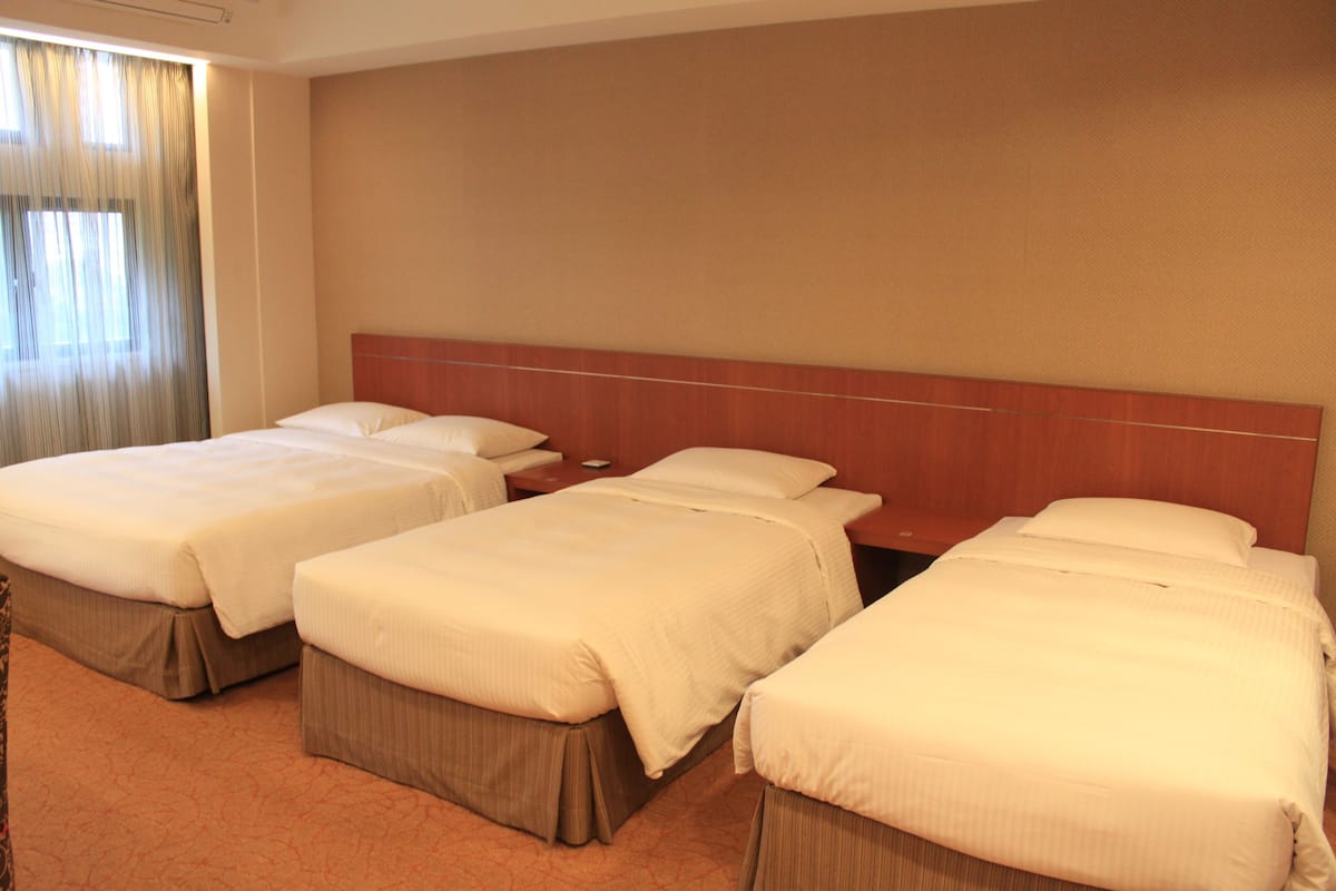 A hotel room with three beds, a wooden headboard, and a carpeted floor.