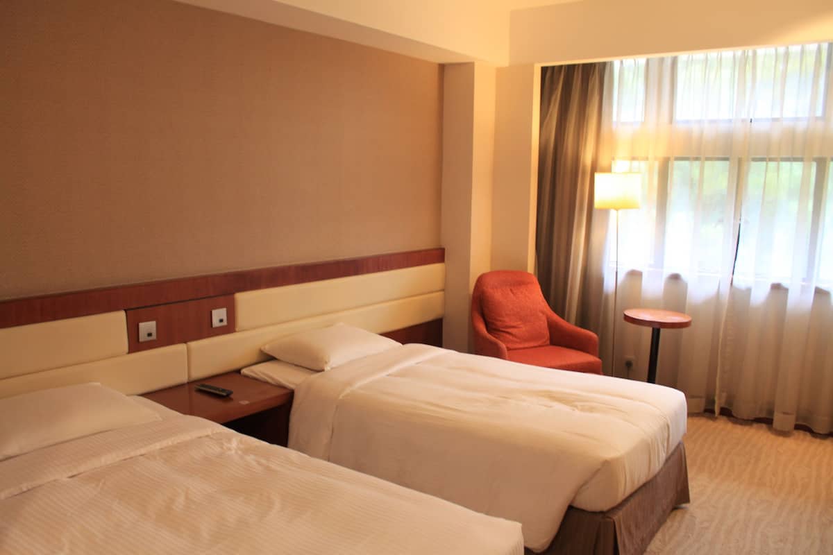 A hotel room with two beds, a nightstand, a chair, a lamp, and a window with curtains.