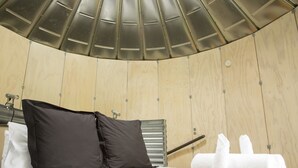 Una habitación de hotel moderna con techo curvo, una cama con ropa de cama blanca, dos almohadas negras y una toalla blanca en el suelo.