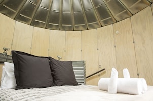 A modern hotel room with a curved ceiling, a bed with white bedding, two black pillows, and a white towel on the floor.