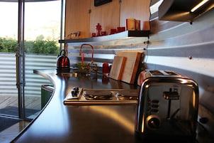 A kitchen with a stainless steel countertop, a kettle, a toaster, and a wooden shelf with kitchenware.