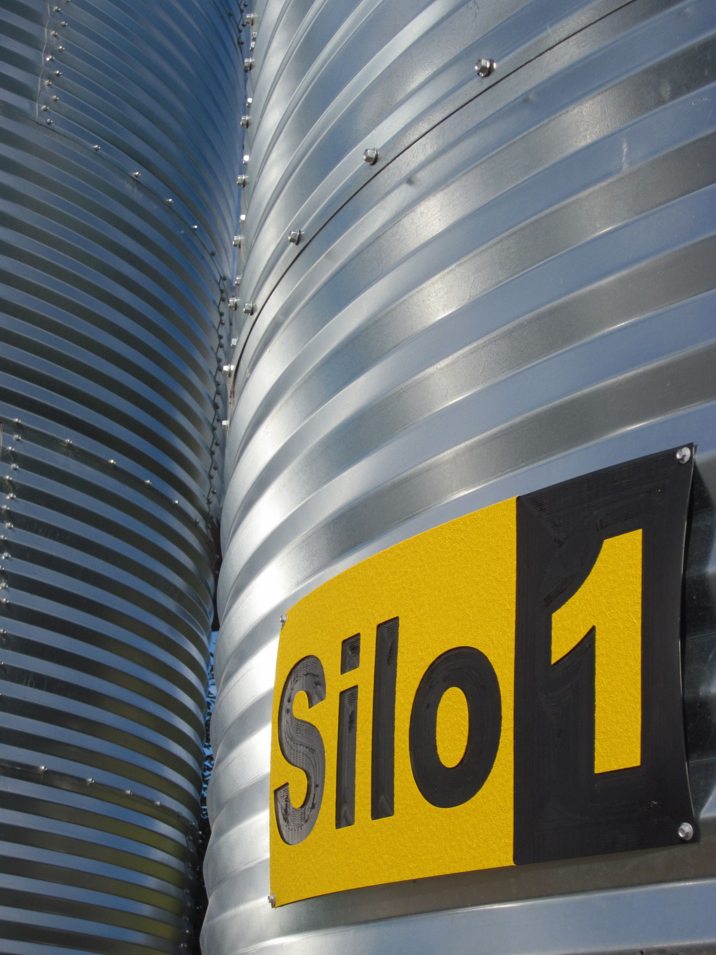 A close-up of a corrugated metal surface with a yellow and black sign reading "Silo 1".