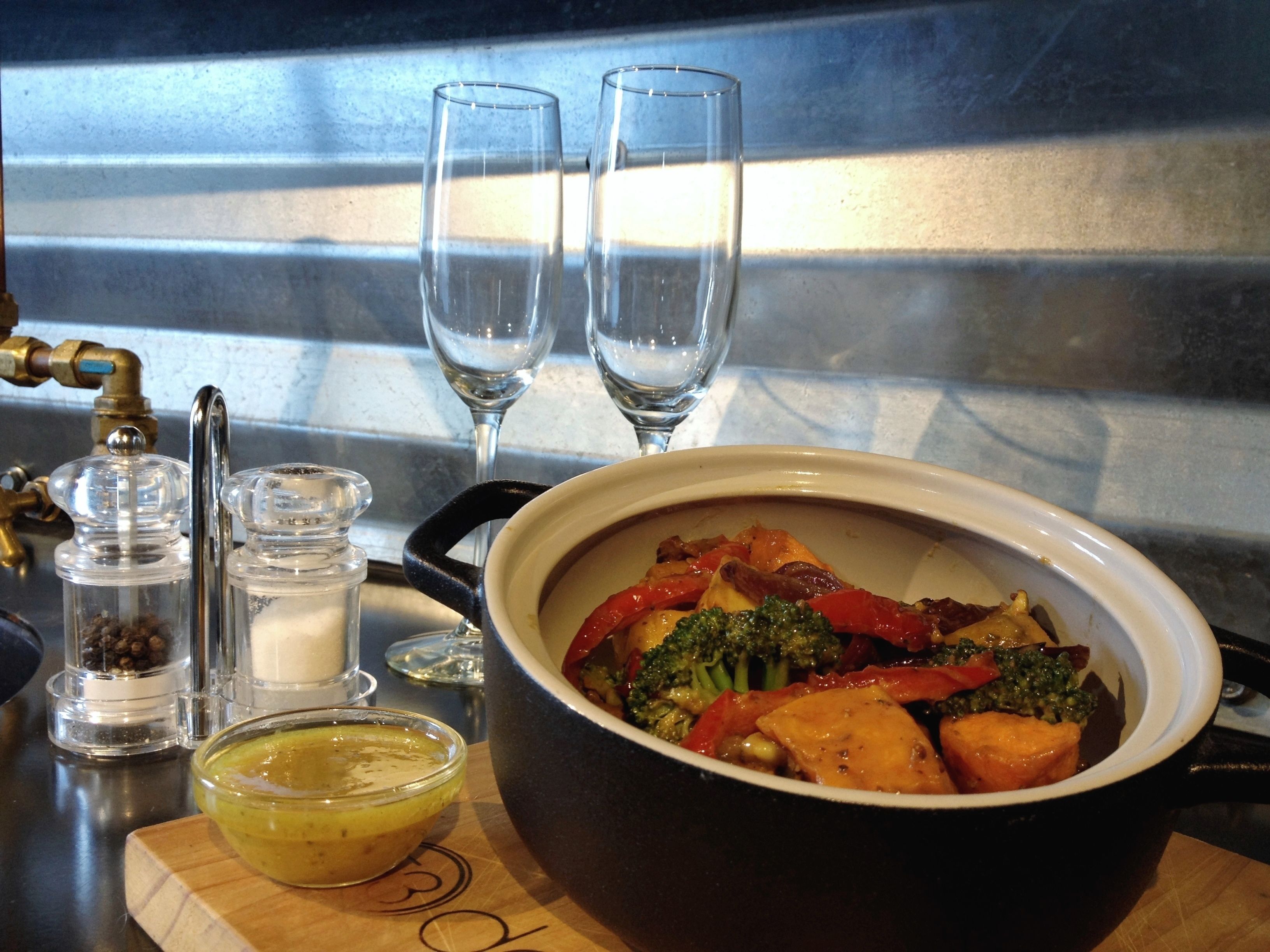A dining table with a bowl of food, two glasses, salt and pepper shakers, and a small bowl of sauce.