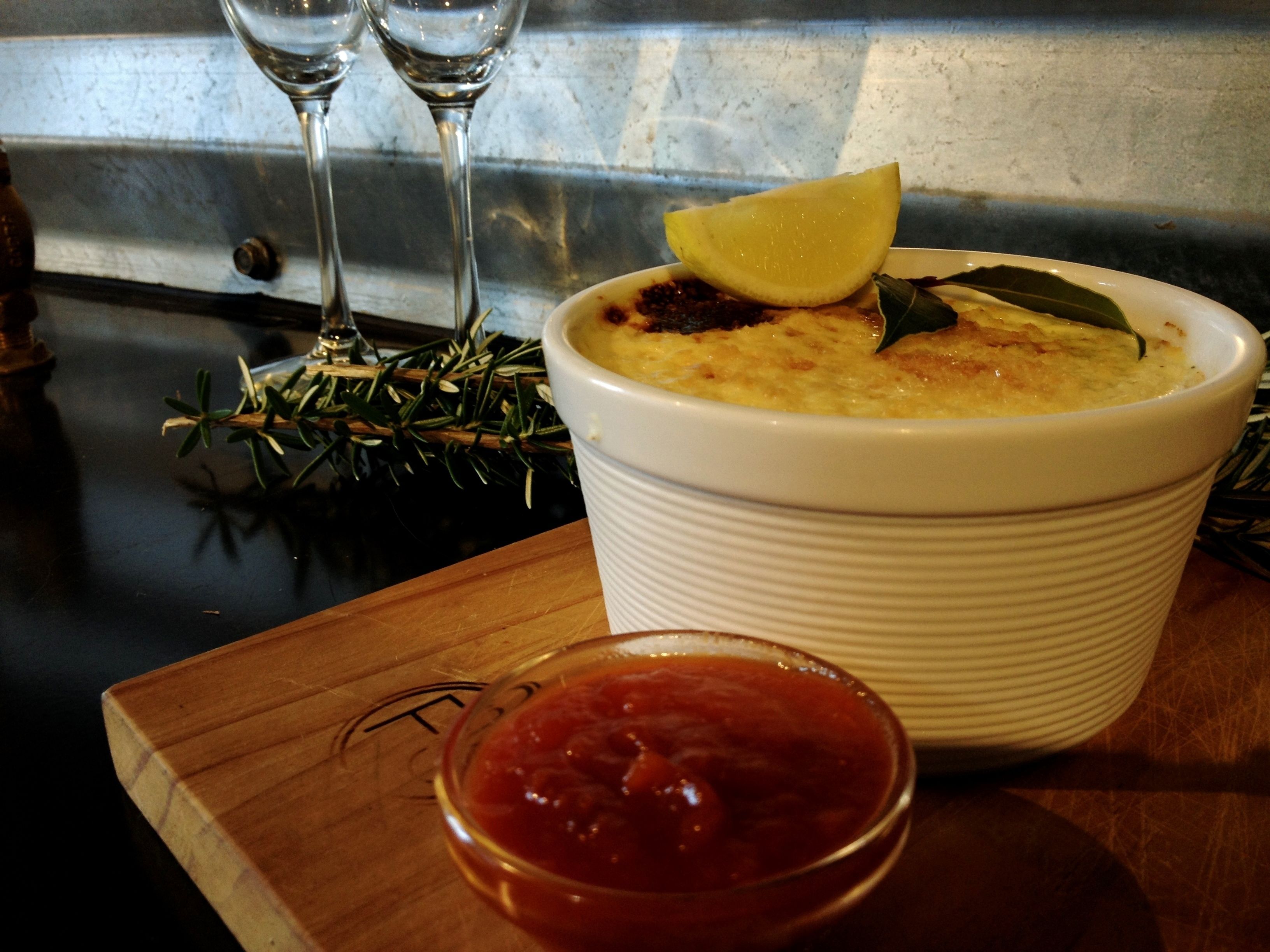 A white bowl of soup with a lemon wedge and a bay leaf on top, placed on a wooden board.