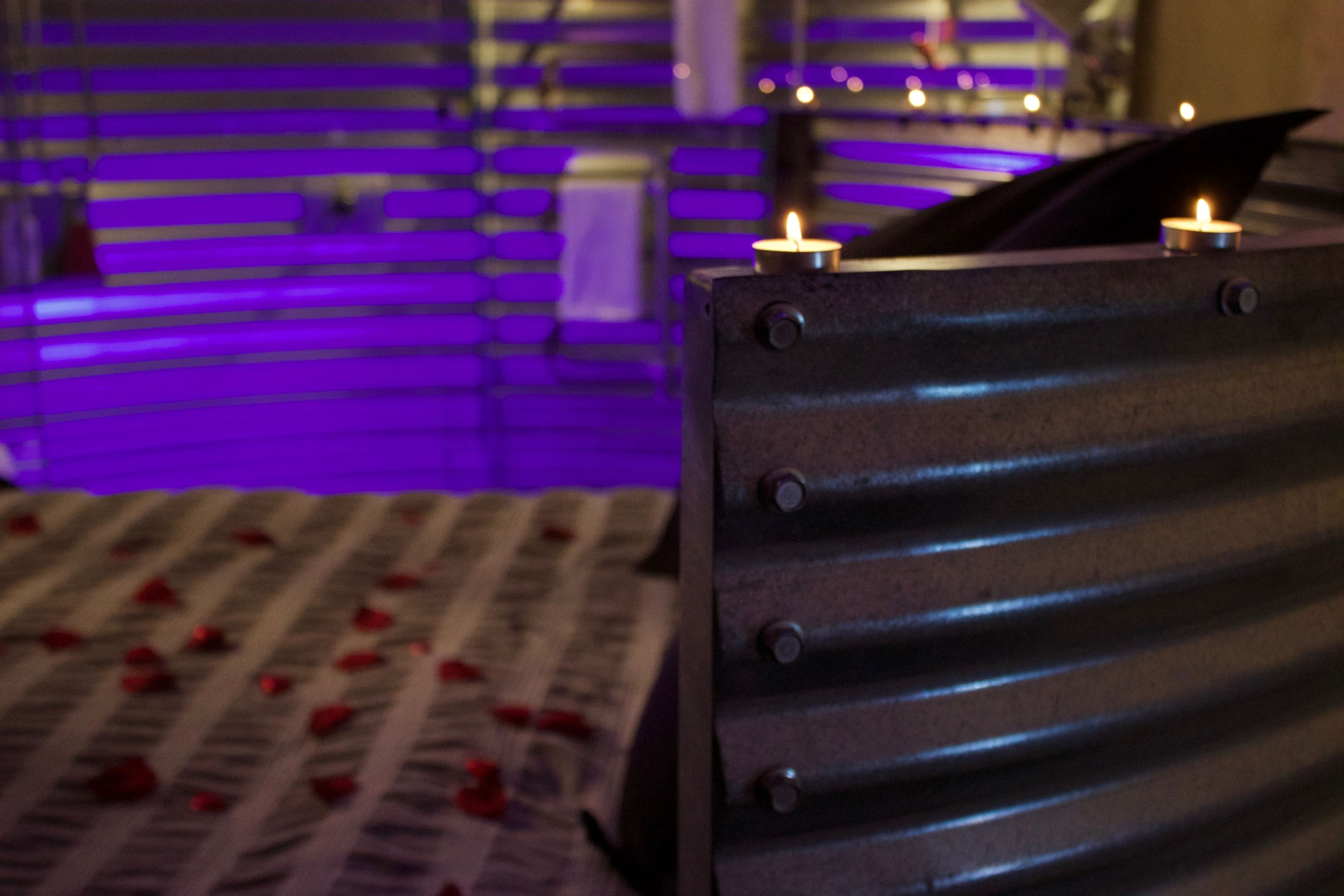 A close-up of a metallic surface with rivets, possibly part of a bed frame or furniture, with a blurred background featuring purple lighting and a candle.