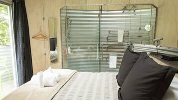 Camera d'albergo con un letto, una cabina doccia in vetro, un armadio in legno e una finestra con tende.