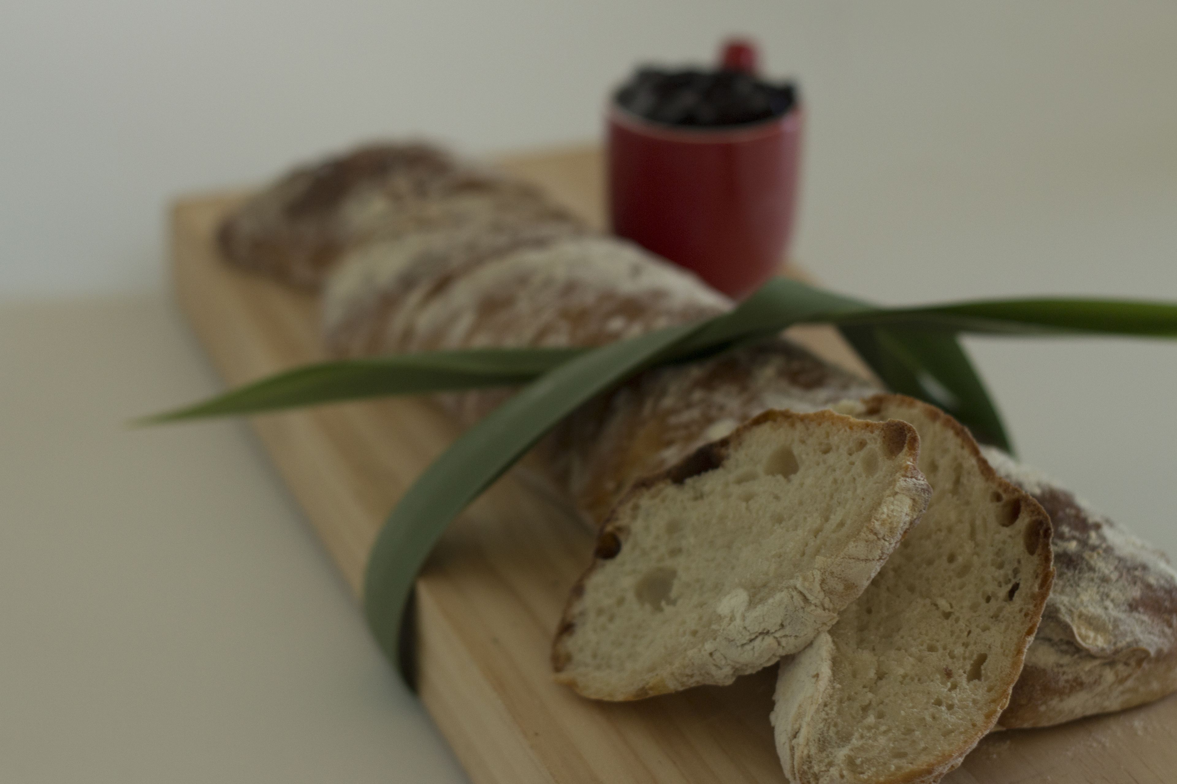 Una barra de pan sobre una tabla de madera con una taza roja al fondo.