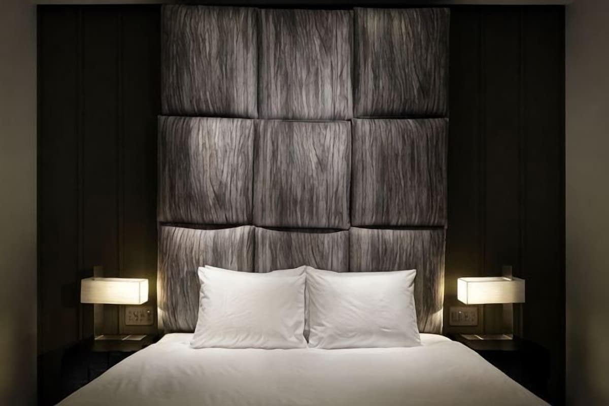 A bed with a large, padded headboard and two bedside lamps.