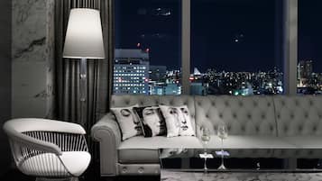 A modern living room with a sofa, a chair, and a large window offering a city view at night.