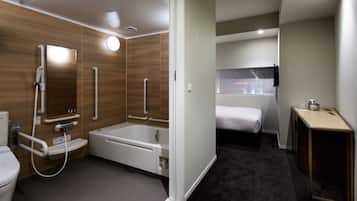 A modern bathroom with a shower, toilet, and bathtub, a bed in the adjacent room, and a small table with a mirror.