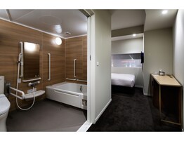 A modern bathroom with a shower, toilet, and bathtub, a bed in the adjacent room, and a small table with a mirror.