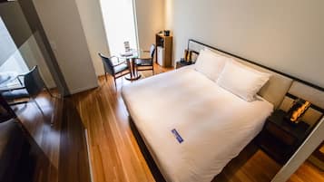 A hotel room with a bed, a desk, a chair, a small table, and a nightstand.