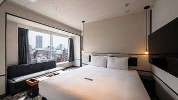 A hotel room with a large bed, a sofa, a TV, and a city view.