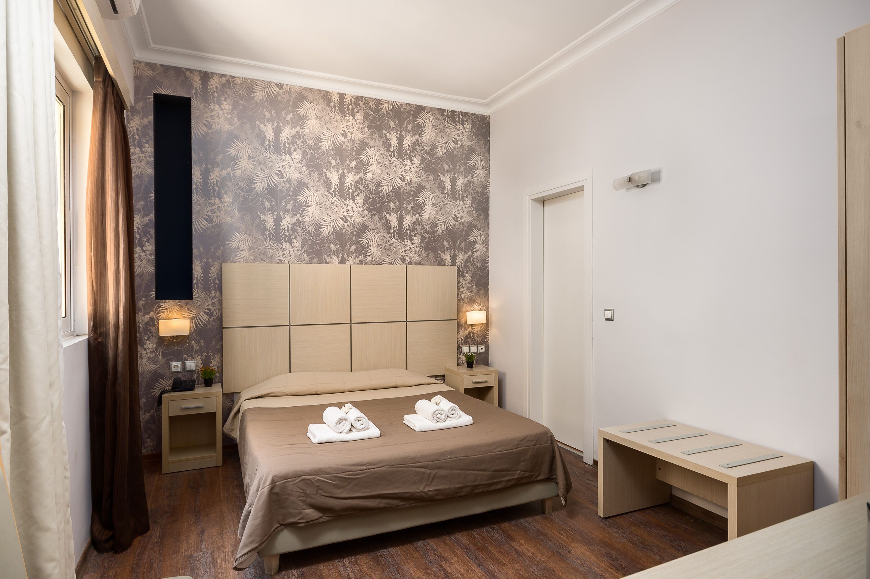 A neatly arranged bedroom with a large bed, bedside tables with lamps, and a bench.