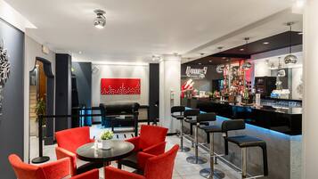 Zona de bar moderna con sillas rojas y una barra, con un adorno en la pared de rojo y blanco, y una variedad de botellas y vasos.