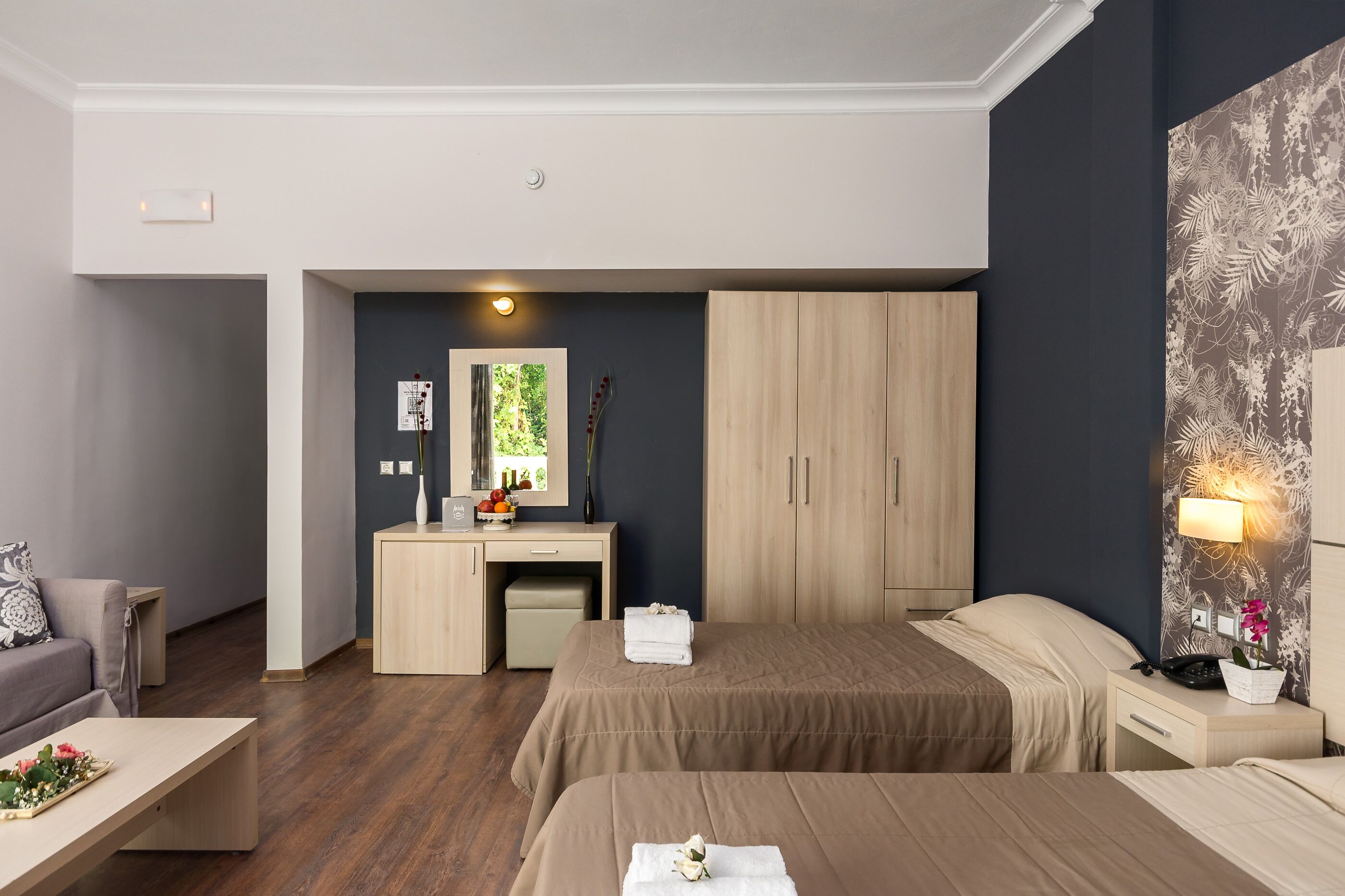 Una habitación de hotel moderna con escritorio, dos camas, un pequeño rincón de descanso y un espejo grande.