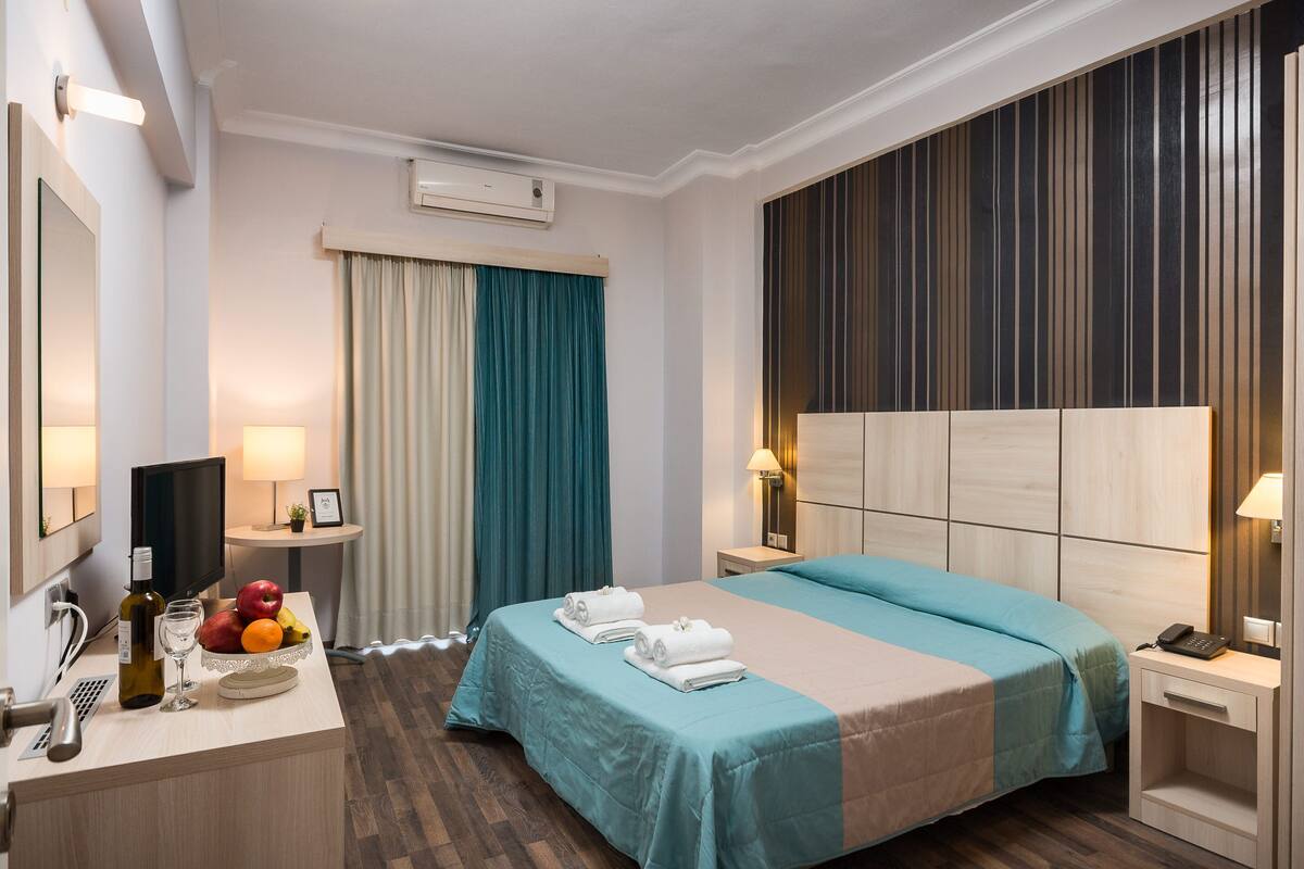 Une chambre d’hôtel comprenant un lit, des tables de chevet, un bureau avec une lampe, une télévision et un panier de fruits.
