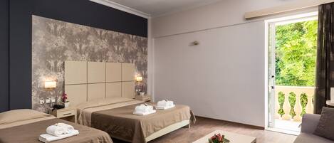 A hotel room with two beds, a small table, and a balcony with a view of greenery.