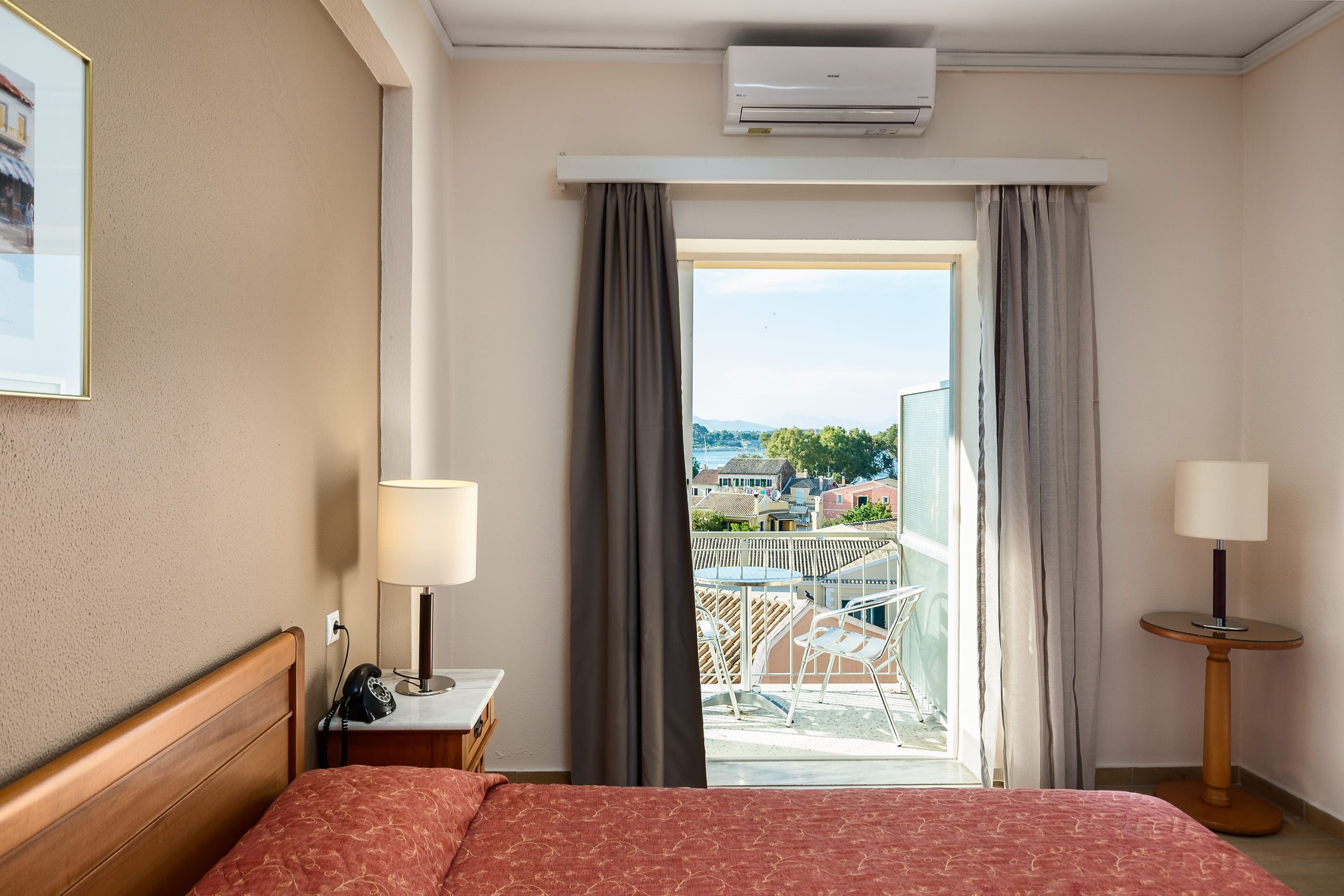 Et hotelværelse med en seng, et natbord, en lampe og udsigt til en balkon.