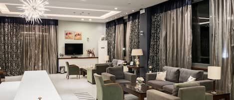 A modern living room with a long white table, grey sofas, and a chandelier.
