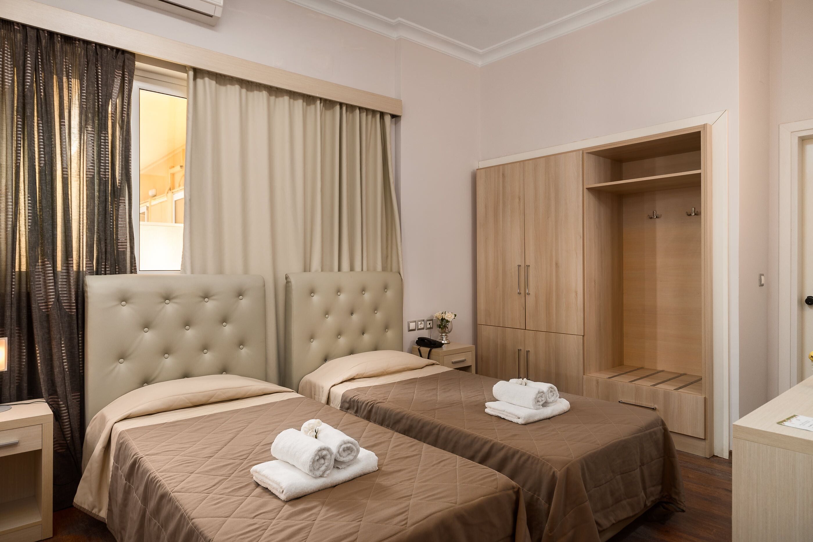 Habitación de hotel con dos camas, un armario, un escritorio y una ventana con cortinas.