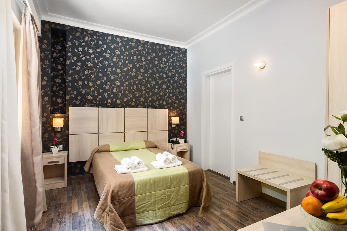 Une chambre d’hôtel comprenant un lit, des tables de chevet, une petite table, un banc et un panier de fruits.