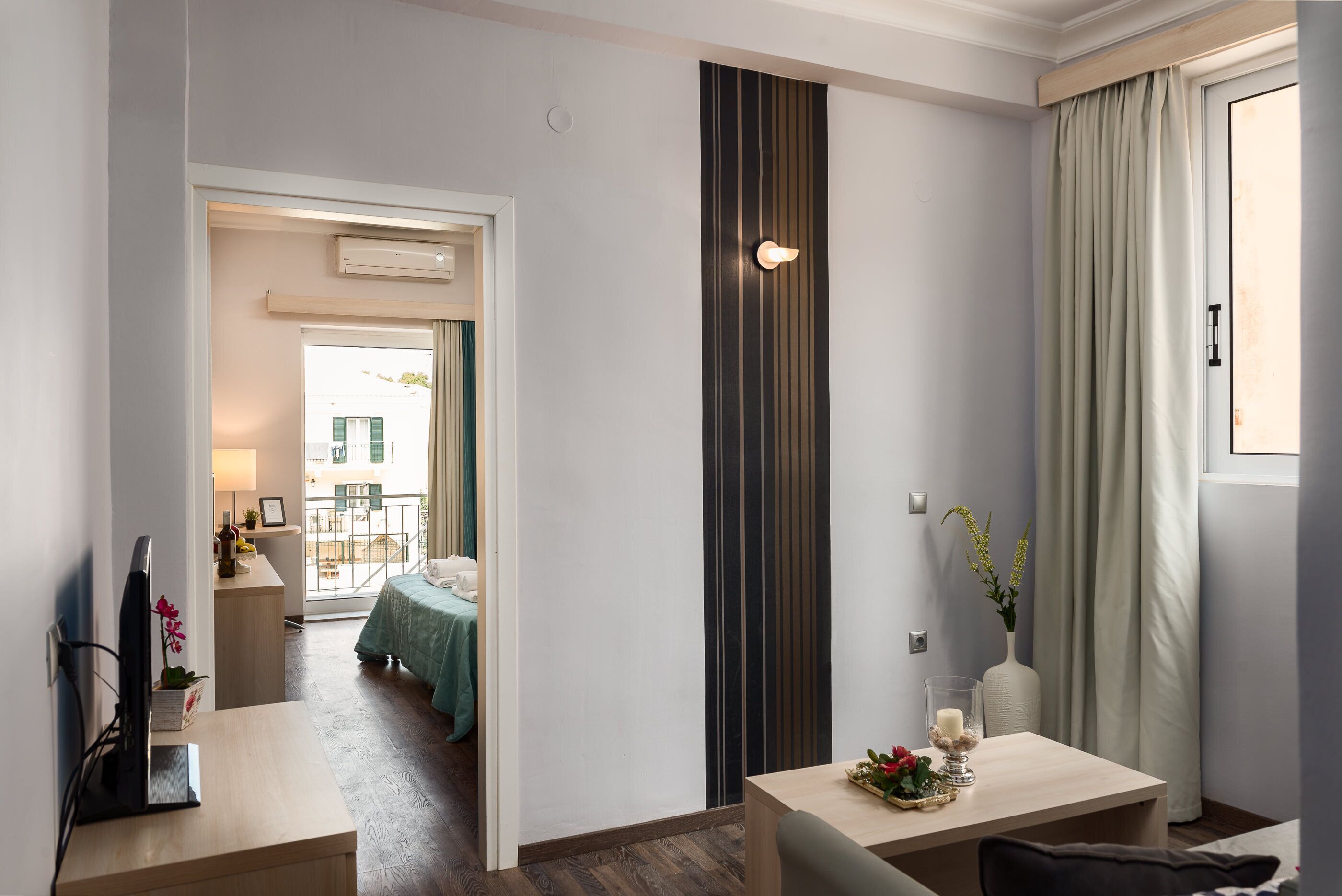 Hotellihuone, jossa on sänky, työpöytä, tuoli, maljakko ja kynttilä varustettu pöytä sekä ikkuna, jossa on verhot.